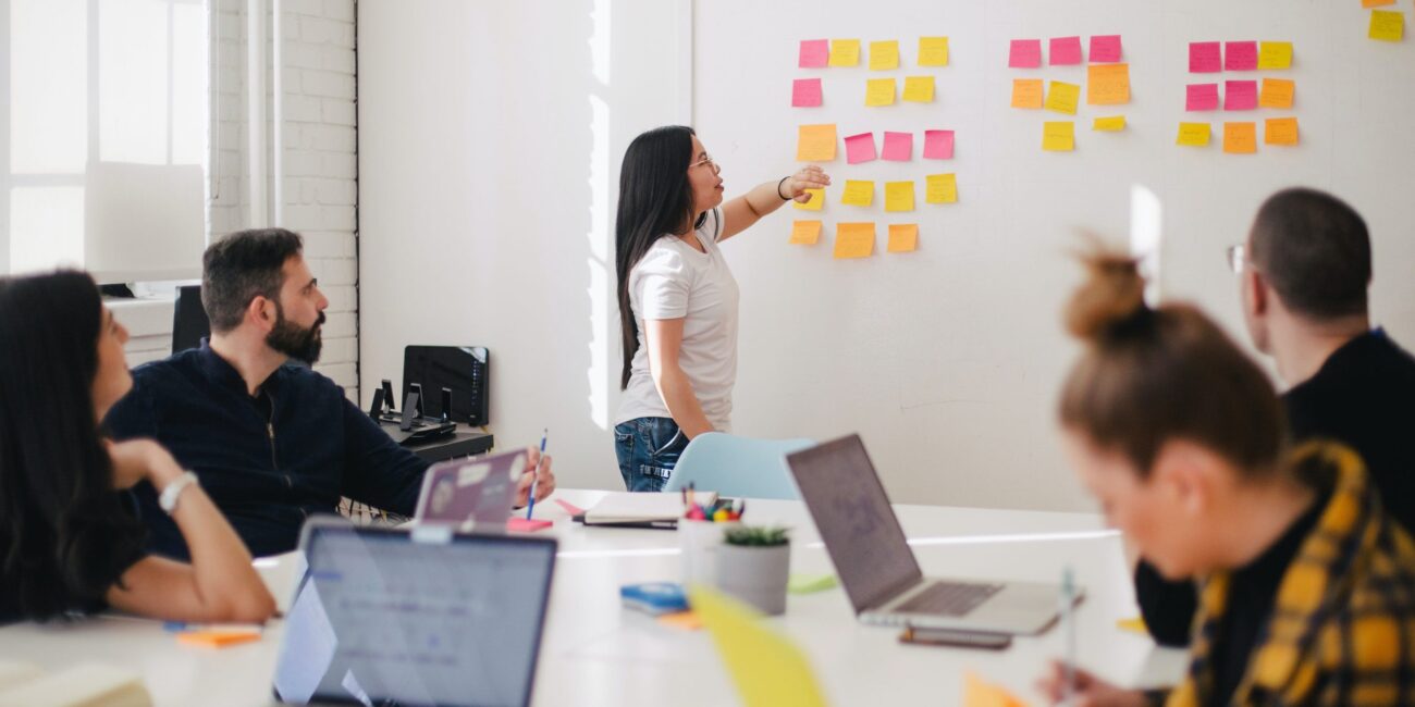 Group of colleagues collaborating while a woman rearranges a series of post-its on the board