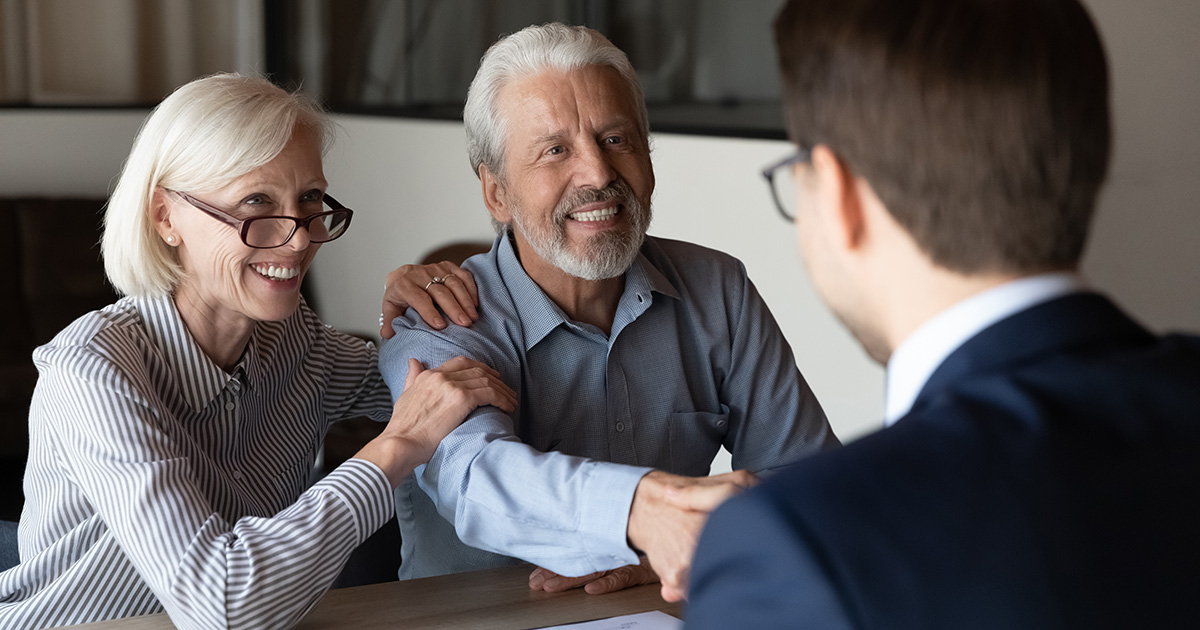 Older couple gleefully shaking hands with a younger gentleman